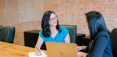 Two women smiling and using computers